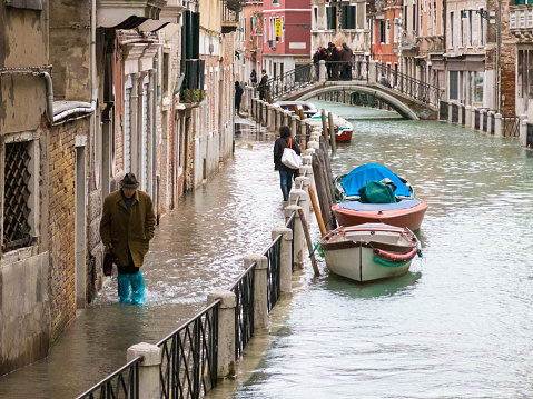 Venice, Italy - February 6, 2015: Elderly man walks along a flooded embankment due to the annual acqua alta in Venice, Italy. 