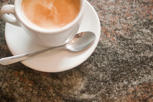 Part of a cup of capuccino served on a granite stone table.