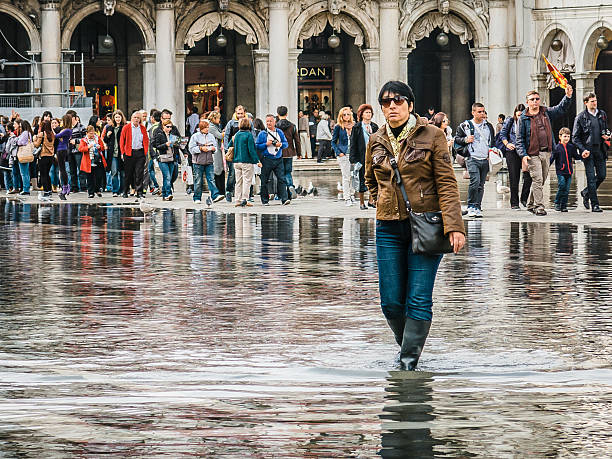 mujer camina a través del acqua alta corriente de waters, st marks. - acqua alta fotografías e imágenes de stock