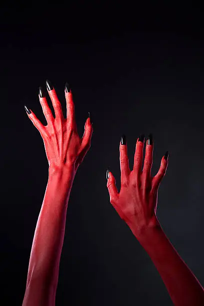 Red devilish hands with black nails, Halloween theme, studio shot on black background