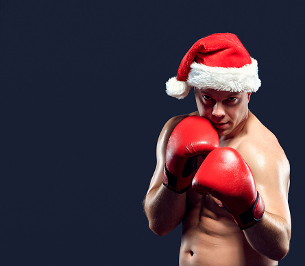 Christmas fitness boxer wearing santa hat and red gloves boxing on black background