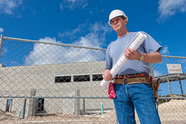 Construction Superintendent Holding Set of Plans on Construction Site A job superintendent holds a set of plans of a building that he is supervising in the background. superintendent stock pictures, royalty-free photos & images