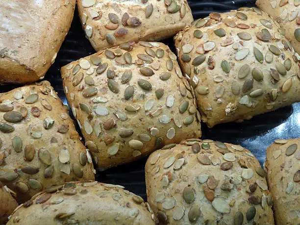 Photo showing a bakery selling square bread rolls, topped with sunflower seeds and almond slices.