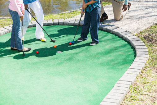 Cropped view of African American family with two children (6 and 9 years) playing miniature golf.