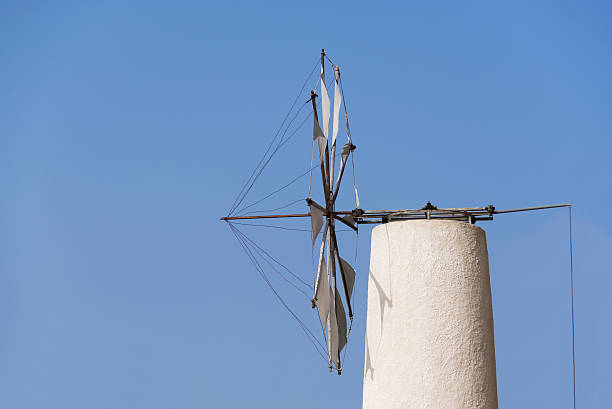 Traditional stone windmill near Toplou Monastery in Crete, Greece, with wooden sails and clear blue sky, historic landmark and cultural heritage site surrounded by Mediterranean trees.