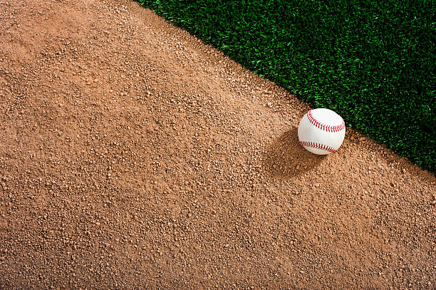 White baseball on a dirt track next to the grass stock photo