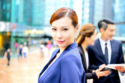Asian woman in suit / dress. More business people and finance district  in background.