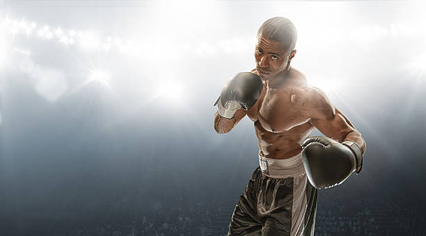 Boxer Ready To Fight Male boxer staring in indoor floodlit boxing venue holding up gloves ready to fight combat sport photos stock pictures, royalty-free photos & images