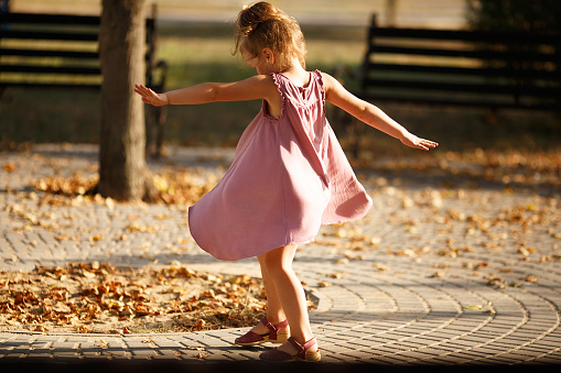 Full length portrait of a little girl dancing in the park a warm autumn evening. In move. Back view