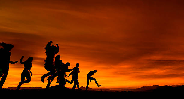 friends silhouettes running on field at sunset.