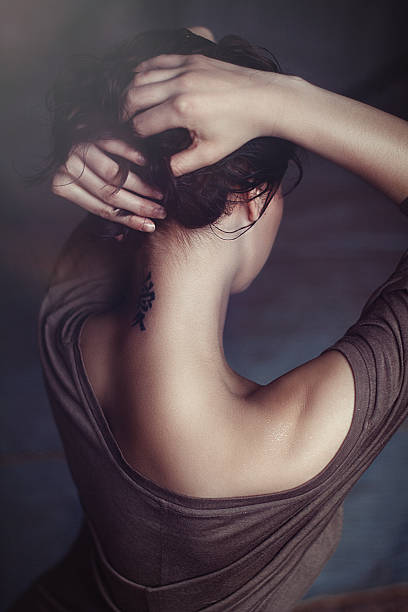 Tattoo on neck Tattoo in the form of hieroglyphs on her neck. The girl in a brown t-shirt stands with his back and holds hands hair gathered on his head. back shoulder tattoos for women pictures stock pictures, royalty-free photos & images