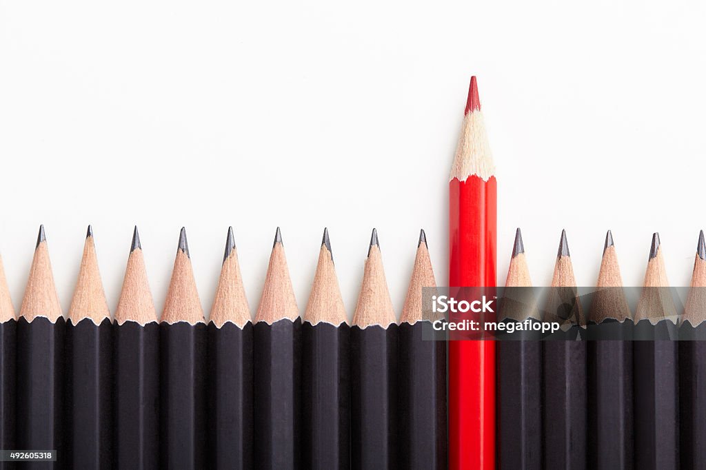 Red pencil standing out from crowd Red pencil standing out from crowd of plenty identical black fellows on white table. Leadership, uniqueness, independence, initiative, strategy, dissent, think different, business success concept Standing Out From The Crowd Stock Photo