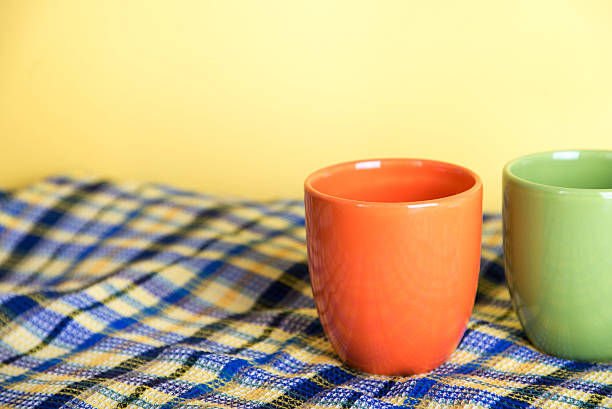 One orange mug and half of green mug standing on a waffle blue towel on a yellow background