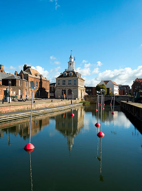 Old Custom House and Purfleet, King's Lynn, Norfolk Kings Lynn, England - September 19, 2015: The Custom House beside the Purfleet in King's Lynn, Norfolk. The Custom House is probably the best-known building in this ancient town and port on the west coast of Norfolk, England. It was built as a merchant exchange in 1683 on reclaimed land at Purfleet Quay in the Dutch style so often seen in Norfolk. The building was bought by the Crown in 1717 for the use of Customs officers and was in use in that capacity until 1989. It is now used as a tourist information office. Buoys are moored in the Purfleet which are topped by seagull-like shapes. (Background people.) kings lynn stock pictures, royalty-free photos & images