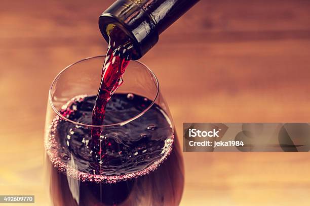 Pouring Red Wine Into The Glass Against Wooden Background Stock Photo - Download Image Now