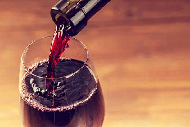 Pouring red wine into the glass against wooden background stock photo