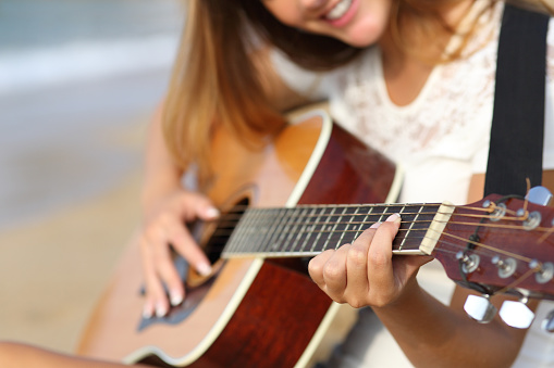 Close up of a woman playing guitar on the beach in a summer sunny day