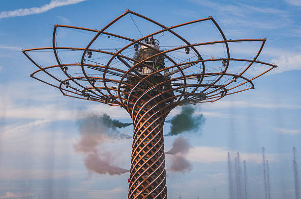 Milan, Italy - October 11, 2015. The tree of life of Expo 2015 in Milano during a colored smoke and fountain show late in the afternoon. The smoke coming out of the tree has the colors of Italian flag, green white and red. The water gushes from the lake on the bottom of the tree. Blue and cloudy sky on the background. 