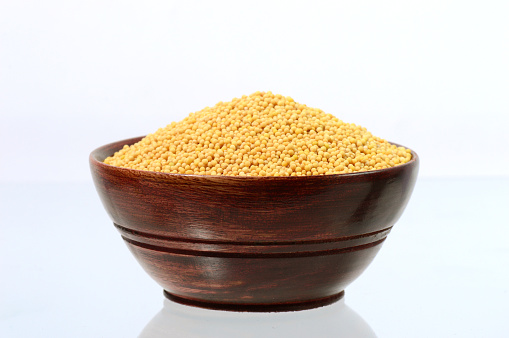 yellow mustard seeds in wooden bowl isolated on white background