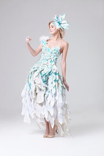 Blond fashion model posing in paper couture gown by Lia Griffith- she's looking down at her finger, which is empty to allow designer to add in a bird or other creature/item. CLICK FOR SIMILAR IMAGES AND LIGHTBOX WITH MORE BEAUTIFUL WOMEN. 
