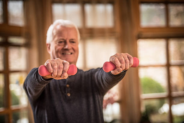 istock Senior man lifting weights in living room 492630990