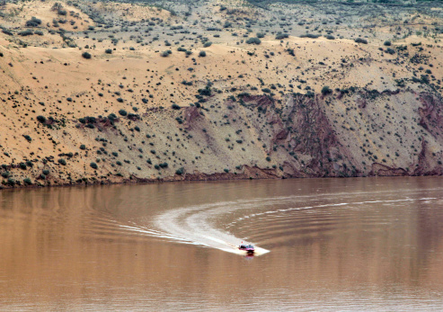 Adult Guy Wake Surfing in Lake Powell during the Day Mountains in the Background Clouds in the Blue Sky