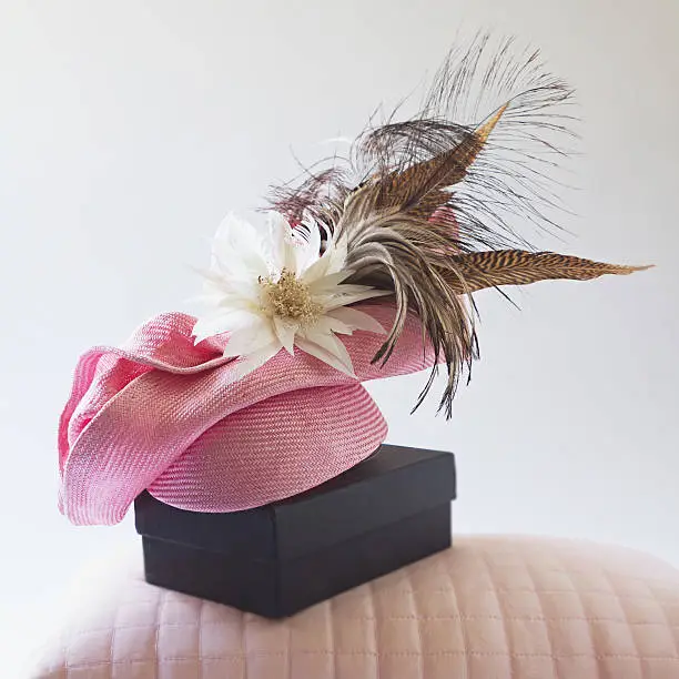 Pink fashion races hat with flower and feathers on a bedroom pillow and box