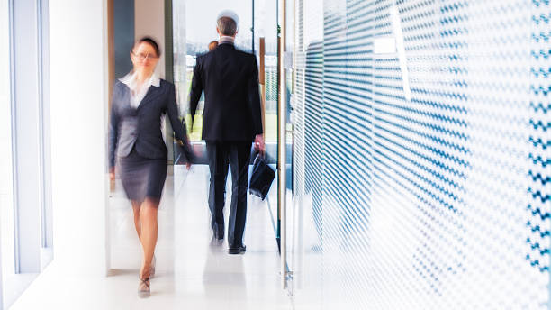Defocused shot of business people walking in modern office corridor Blurred motion shot of two businesspeople passing by each other in a modern office corridor. walking into glass door stock pictures, royalty-free photos & images
