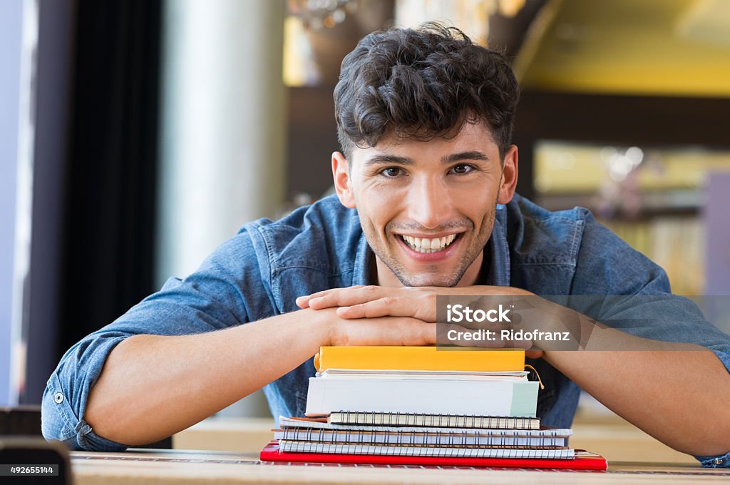 Young man leans on stack of books Closeup shot of young man leans on stack of books. Happy male student smiling and looking at camera. Lughing guy leaning on a pile of books and school notebooks. University Student Stock Photo