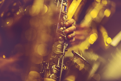 A brass band is playing in the city park. Vertical close-up images of a group of saxophonists in the foreground.