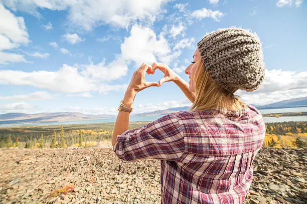 Young cheerful woman enjoying nature in Autumn season. She is making a heart shape with her hands.