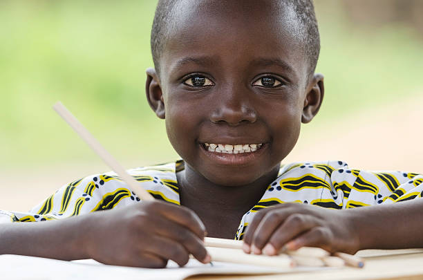 Handsome Little African Black Boy Toothy Smile in School Writing Writing little black African ethnicity boy. Handsome young African man close-up shot. Beautiful toothy smile on his face outdoors his school sitting in his desk learning his lesson. sad african child drawings stock pictures, royalty-free photos & images