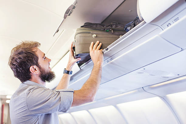 istock man putting luggage on the top shelf on airplane 492672368