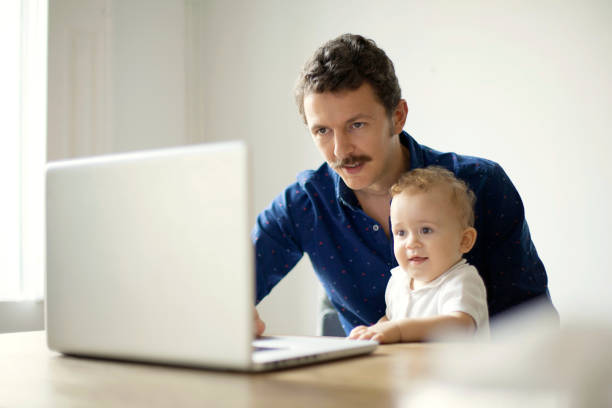 istock Man at desk with baby and computer 492674308
