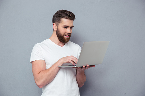 Portrait of a smiling casual man using laptop computer over gray background