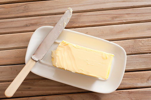 Pat of fresh farm butter on a butter dish with a knife to use as a spread or cooing ingredient, overhead view on a slatted wooden table