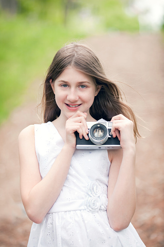 A beautiful 12 year old girl holding a vintage camera outdoors.