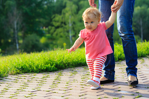 first steps of little girl with mother outdoors, kids learning
