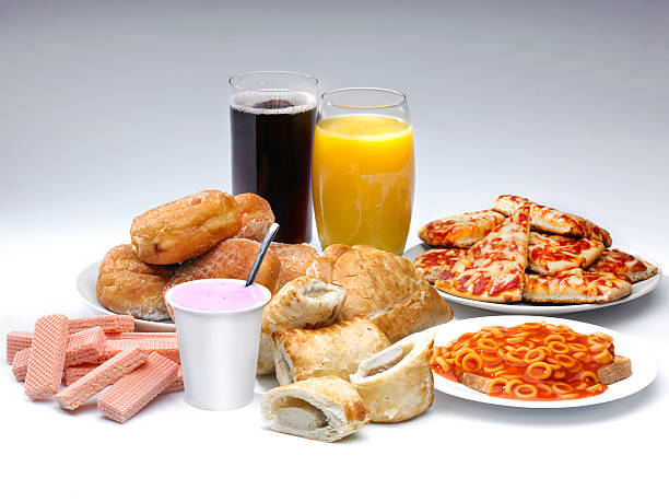 Food A selection of processed food and drink on a white background including pIzza, cola, buscuits and sausage rolls convenience food photos stock pictures, royalty-free photos & images