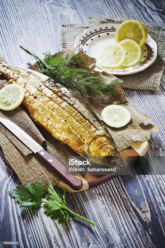 smoked fish with lemon, dill and parsley smoked fish with lemon, dill and parsley on a wooden background. whitefish Smoked Food Stock Photo