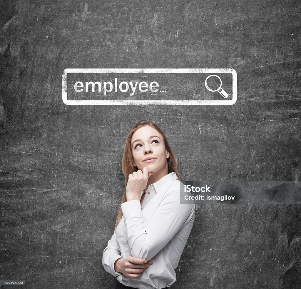 recruiter is looking for new employees in Internet A beautiful recruiter by holding her chin is looking for new employees in the Internet. Internet concept of search available candidates. Black chalk board on the background. 2015 Stock Photo