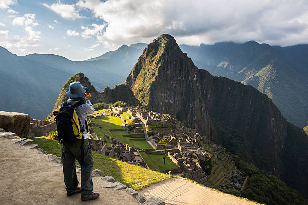 Photographing Machu Picchu with smartphone Tourist photographing Machu Picchu illuminated by the last sunlight from above with smartphone. Scenic sky with clouds and sun rays. Concept of sharing travel moments using technology. machu picchu photos stock pictures, royalty-free photos & images
