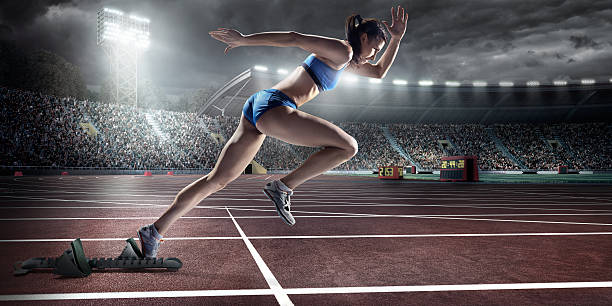 Female athlete sprinting Professional female athlete sprinting from blocks on numbered start line on outdoor athletics track on . stadium full of spectators under a dramatic evening sky. Sprinter is wearing generic athletics kit. all weather running track stock pictures, royalty-free photos & images