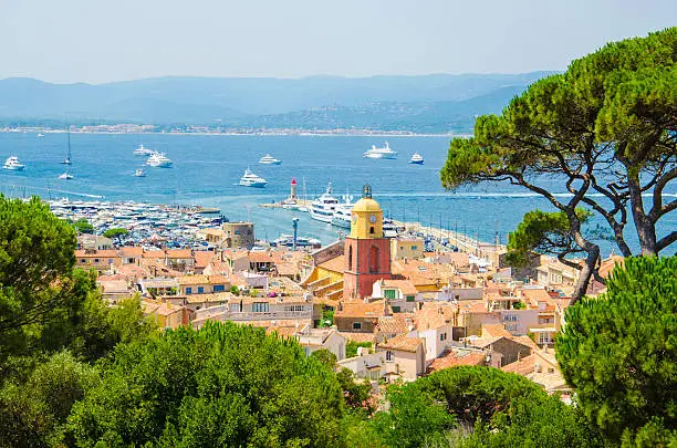 Looking from a viewpoint at the view of the town of Saint Tropez in France. St Tropez is a popular French summer holiday resort. The colour image was taken on a hot summer day. St.-Tropez is a coastal town on the French Riviera, in the Provence-Alpes-Côte d'Azur region of southeastern France. Long popular with artists, the town attracted the international "jet set" in the 1960s, and remains known for its beaches and nightlife. The cobblestoned La Ponche quarter recalls its past as a fishing village, although yachts now outnumber fishing boats in the Vieux Port.