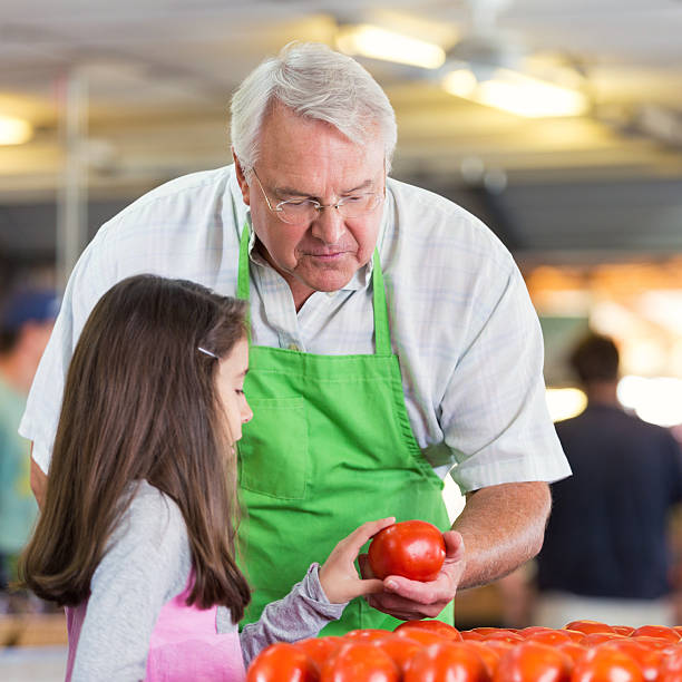 proprietario del negozio di alimentari insegnando ai giovani il cliente a scegliere prodotti - market farmers market agricultural fair child foto e immagini stock