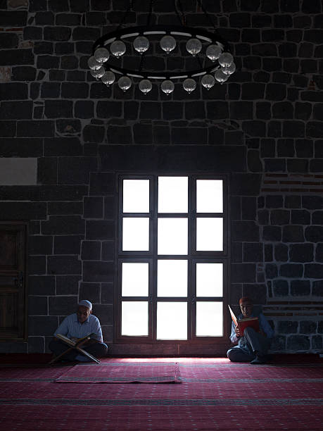 People Reading Holy Koran Inside Ulu Cami In Diyarbakir Diyarbakir, Turkey - August 13, 2014: People Reading Holy Koran Inside Ulu Cami In Diyarbakir (The Great Mosque of Diyarbakir) in Diyarbakir,Turkey.The carpet is red and walls are made of black stones.Two senior men each is sitting on each side of large window in the middle of frame.Shot with a full frame DSLR camera.The mosque is accepted as the oldest mosque in Anatolia. ulu camii stock pictures, royalty-free photos & images