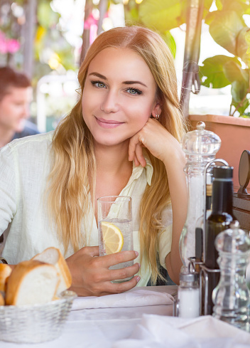 Portrait of beautiful blond woman sitting at outdoors cafe and drink water with lemon, healthy nutrition, traveling to Italy, Europe