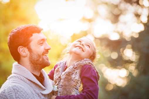 Father and daughter enjoying outdoors on a sunny autumn day. Sun is shining from behind.