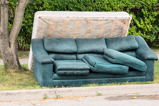 A mattress and couch placed outside by the curb on garbage day.