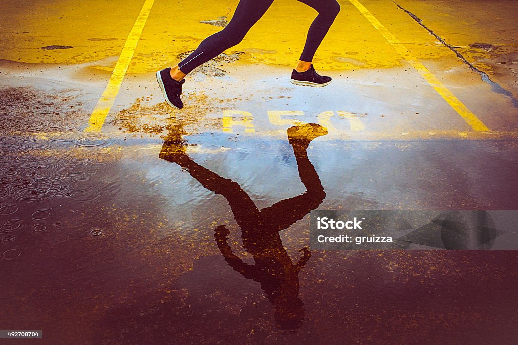 Young person running over the parking lot Young person running over the yellow parking lot. Black sport clothing - sport shoes, running tights, and a jacket. High angle view of a runner's legs and its reflection in the water. Running Stock Photo